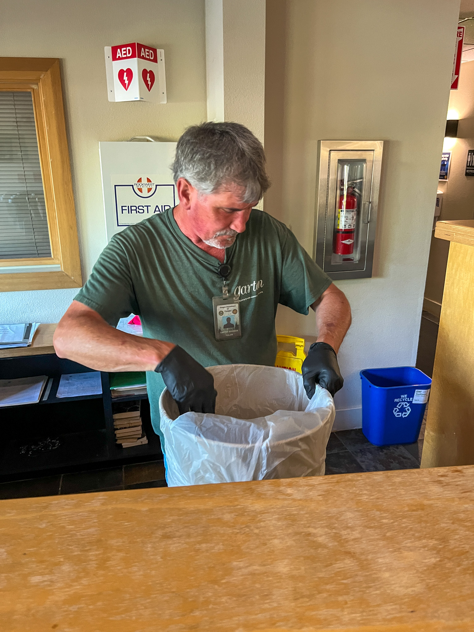 Commercial cleaning staff emptying trash bins and replacing liners in a building.